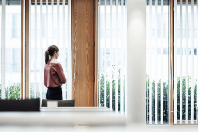 Businesswoman looking through window while standing in office