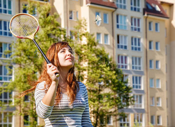 Beautiful young woman playing badminton against building