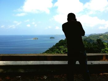 Rear view of man standing by sea against sky