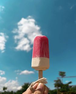 Cropped hand of person holding ice cream cone against sky