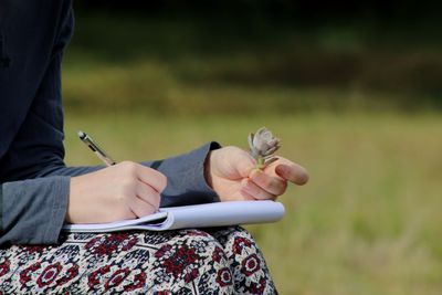 Midsection of woman holding plant while writing in note pad