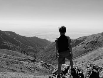 Rear view of man standing on mountain against clear sky