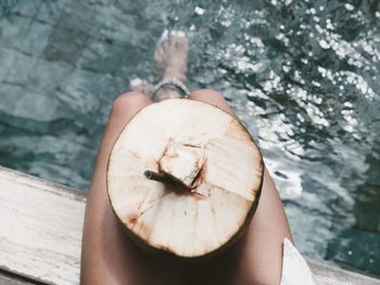 Low section of woman with coconut sitting on pier