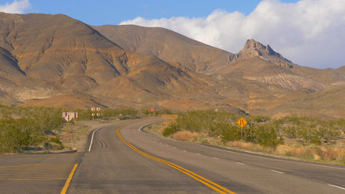 Country road by mountains against sky