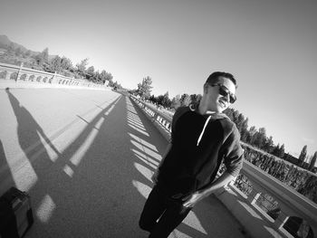 Teenage boy looking away while standing on road in city against sky