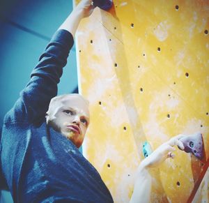 Low angle view of athlete making face while climbing rock wall in gym