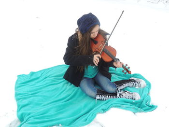 Full length of woman playing violin on fabric at snow covered field