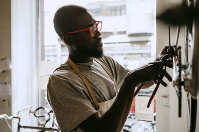 Male owner with hand tool repairing bicycle in workshop