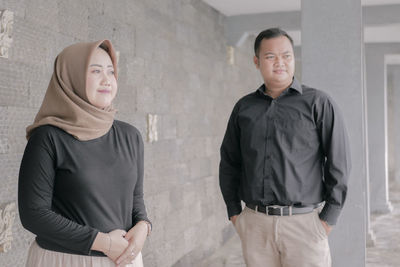 Young couple looking away while standing against wall