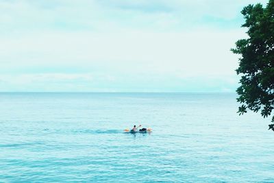 People rowing boat in sea against sky