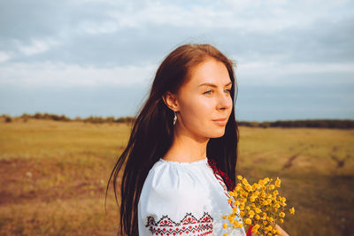 Beautiful young woman in a ukrainian embroidered shirt walking in the field with yellow flowers