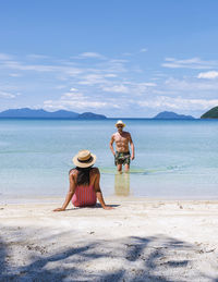 Rear view of woman sitting at beach against sky