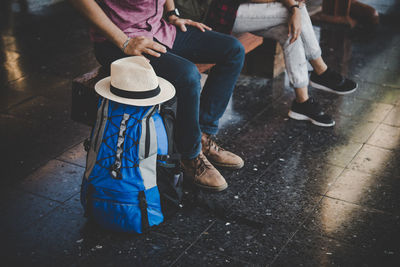 Low section of man sitting on bench by backpack and hat 