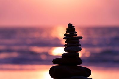 Stack of pebbles on beach against sky during sunset