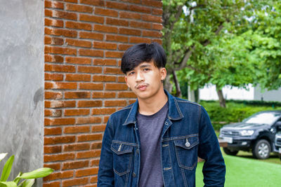 Portrait of young man standing against brick wall