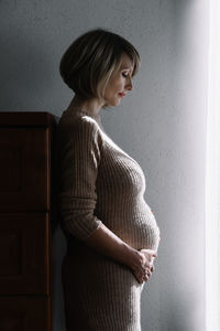 Woman looking away while standing against wall at home