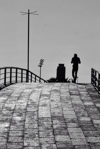 Silhouette man walking on road against clear sky