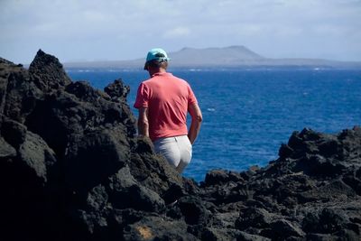 Rear view of man standing on rocks by sea