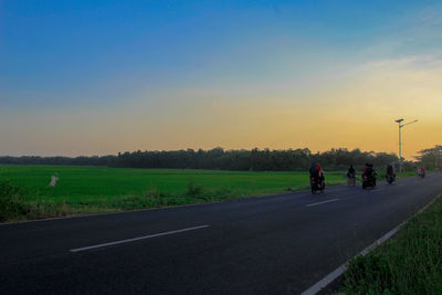 People riding motorcycle on road against sky during sunset