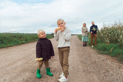 Family walking in corn field at autumn, kids eating corncob