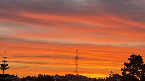 Silhouette of electricity pylons against orange sky