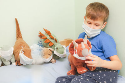 Child plays role-playing games. baby bay and his dinosaurs toys wearing medical mask 