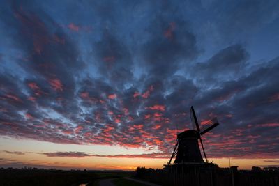 Traditional windmill against cloudy sky during sunset