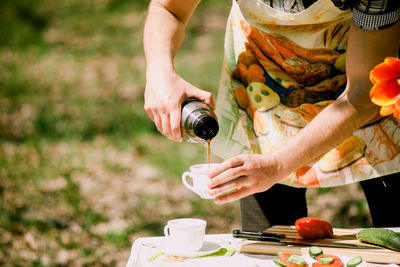 Midsection of man pouring tea in cup outdoors