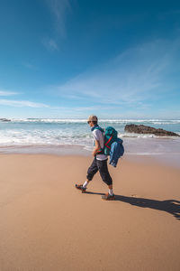 Rear view of woman walking at beach against sky