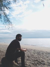 Side view of young man sitting on beach