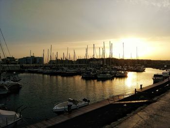 Sailboats moored in harbor at sunset