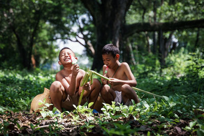 Full length of shirtless man sitting in forest