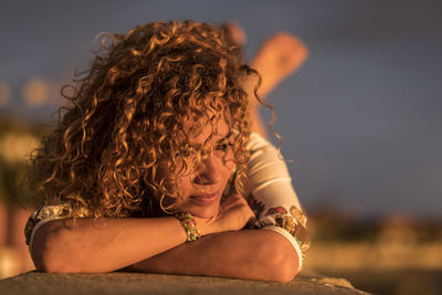 Close-up of thoughtful woman lying on railing during sunset