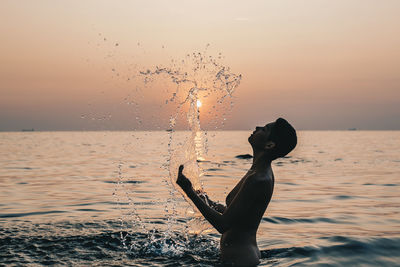 Silhouette man splashing in sea against sky during sunset