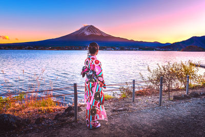 Side view of woman standing by lake against mountain and sky