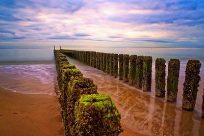 Wooden posts on beach against sky during sunset