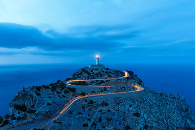 Illuminated lighthouse by sea against sky