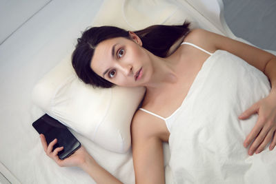 Brunette woman with a phone is lying on the bed and can not fall asleep from insomnia