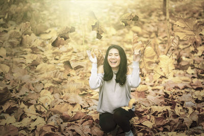 Portrait of smiling young woman standing by autumn leaves