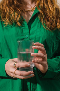Close-up of unrecognizable woman in bright green shirt holding trendy fluted glass with clean water.