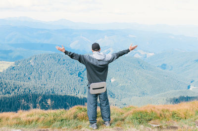 Rear view of hiker with arms outstretched standing on mountain