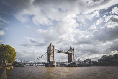 Tower bridge over thames river in city against cloudy sky