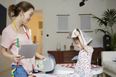 Fashion designer with digital tablet looking at playful daughter holding textile