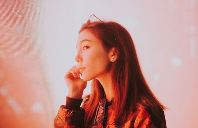 Close-up of young woman standing against illuminated city at night