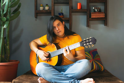 Man with long hair playing acoustic guitar at home during quarantine