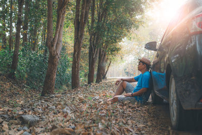 Woman sitting on sidewalk by trees in forest during autumn