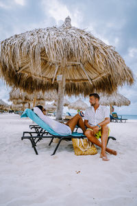 Man sitting on chair at beach against sky
