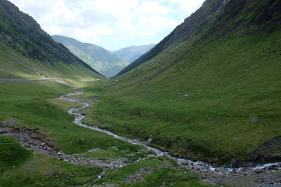 Scenic view of stream amidst green landscape against sky