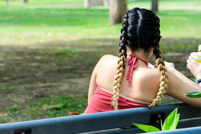 Rear view of woman with braided hair resting on bench at park