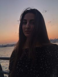 Portrait of a beautiful young woman against sea during sunset